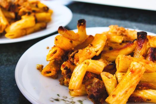 Penne pasta tubes with bolognese sauce on a white plate on a kitchen worktop