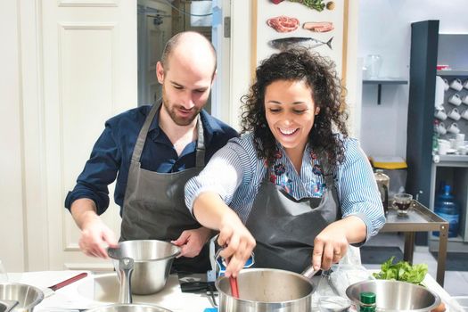 A young couple enjoying cooking together in the kitchen wearing aprons