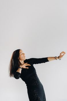 A girl in a black dress moves in a dance on a gray background. Dynamic dance,