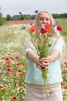 a beautiful middle-aged blonde woman stands among a flowering field of poppy, daisies, Cornflowers, and holds a bouquet of wild flowers and laughs. High quality photo