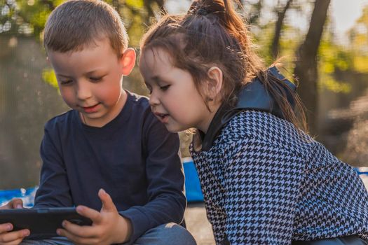 children sit on a trampoline and look at the phone