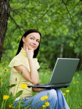 Young woman sitting on the grass with laptop on her knees and thinking about the future or past.