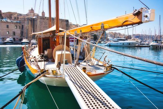 A luxury sailboat moored in a Mediterranean harbor with the gangplank extended