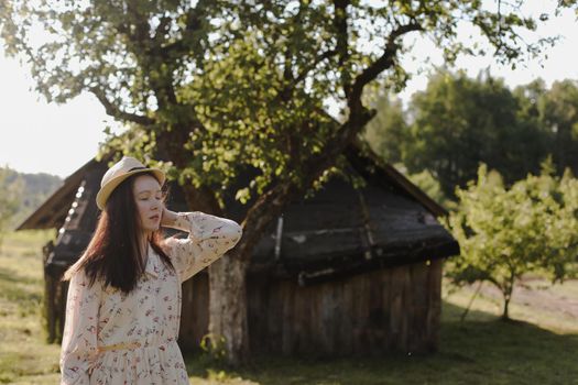 romantic portrait of a young woman in straw hat and beautiful dress in the countryside in summer.