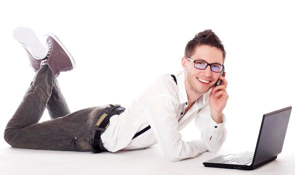 Businessman lying in front of laptop and calling on mobile phone. Isolated against a white background.
