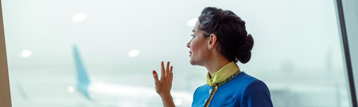 Female flight attendant in aviation air hostess uniform looking out the window and enjoying airfield view