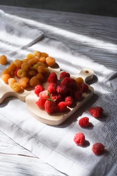 Two handfuls of fresh red and yellow raspberry on white wooden kitchen boards, sselectivew focus, hard light with copy space.