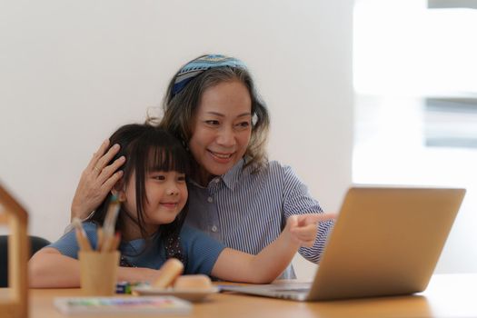 Happy moments of Asian grandmother with her granddaughter using video call. Leisure activities for children at home