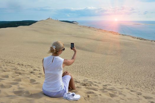 Blonde girl making selfie for instagram at Pyla dune, the largest sand dune in Europe, France