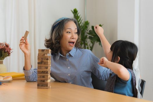 Happy moments of Asian grandmother with her granddaughter playing jenga constructor. Leisure activities for children at home