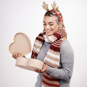 Studio shot of an attractive young woman opening a heart-shaped boxed while dressed in Christmas-themed attire.