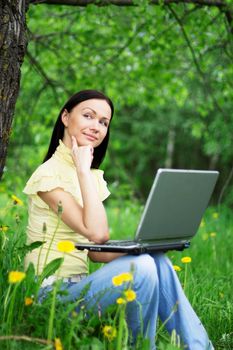 Young woman sitting on the grass with laptop on her knees and thinking about the future or past.