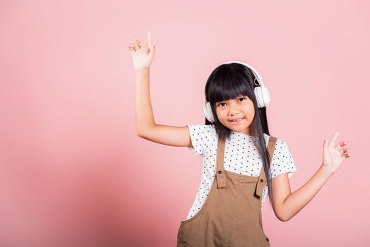 Asian little kid 10 years old smiling listening music wearing wireless headset and dancing in studio shot isolated on pink background, Child girl funny listen music with headphones