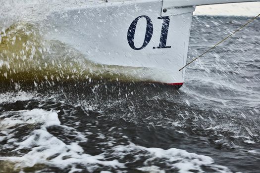 the bow of the boat cuts through the water, bowsprit of sailing yacht in sailing regatta at stormy weather, splashes of water, hot racing, number one. High quality photo