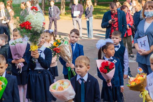 NOVOKUZNETSK, KEMEROVO REGION, RUSSIA - SEP, 1, 2021: Meeting with the first-grade pupils and teacher at schoolyard. The day of knowledge in Russia.