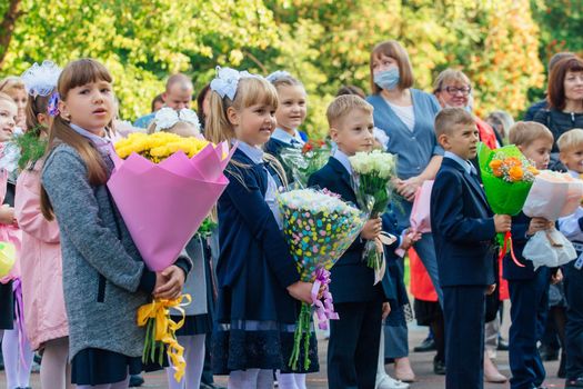 NOVOKUZNETSK, KEMEROVO REGION, RUSSIA - SEP, 1, 2021: Meeting with the first-grade pupils and teacher at schoolyard. The day of knowledge in Russia.