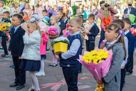 NOVOKUZNETSK, KEMEROVO REGION, RUSSIA - SEP, 1, 2021: Meeting with the first-grade pupils and teacher at schoolyard. The day of knowledge in Russia.