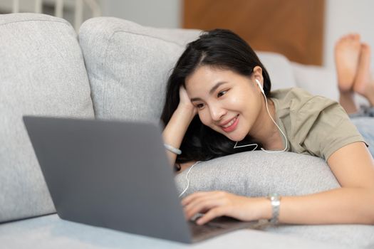 Relaxed woman using laptop in living room, enjoying working, internet shopping, checking social network, reading news or communicating online with computer laying on sofa.