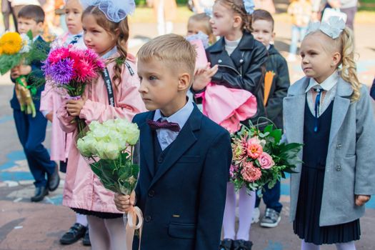 NOVOKUZNETSK, KEMEROVO REGION, RUSSIA - SEP, 1, 2021: Meeting with the first-grade pupils and teacher at schoolyard. The day of knowledge in Russia.