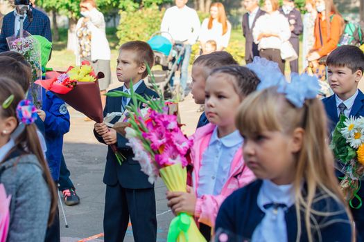 NOVOKUZNETSK, KEMEROVO REGION, RUSSIA - SEP, 1, 2021: Meeting with the first-grade pupils and teacher at schoolyard. The day of knowledge in Russia.