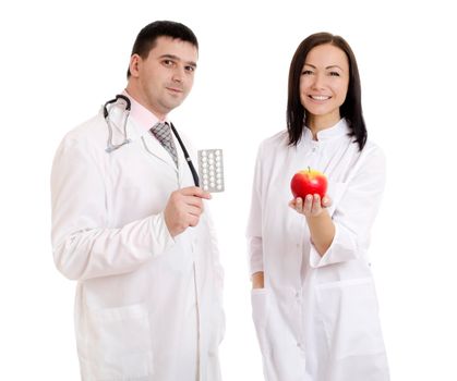 Male and female doctors holding apple and bunch of tablets isolated on white background