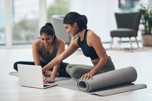 Shot of two young women using a laptop while working out at home.