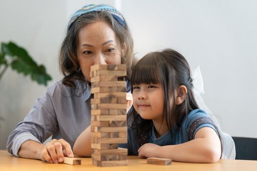 Happy moments of Asian grandmother with her granddaughter playing jenga constructor. Leisure activities for children at home