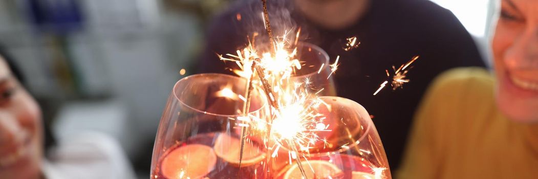 Group of people is holding glasses with cocktail with alcohol and sparklers. Christmas party concept