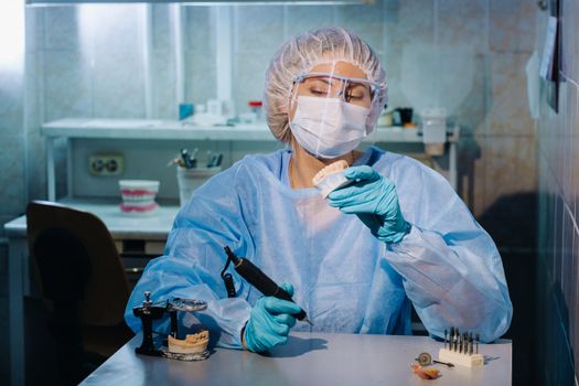 A dental technician in protective clothing is working on a prosthetic tooth in his laboratory.