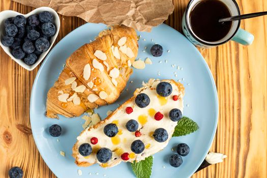 classic american breakfast. Fresh french croissant with fresh berries. blueberry and strawberry on cream cheese. Croissant and a cup with the inscription coffee on wooden background. Healthy breakfast