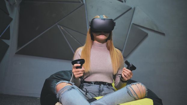 A teenage girl sits in a club with virtual glasses and plays