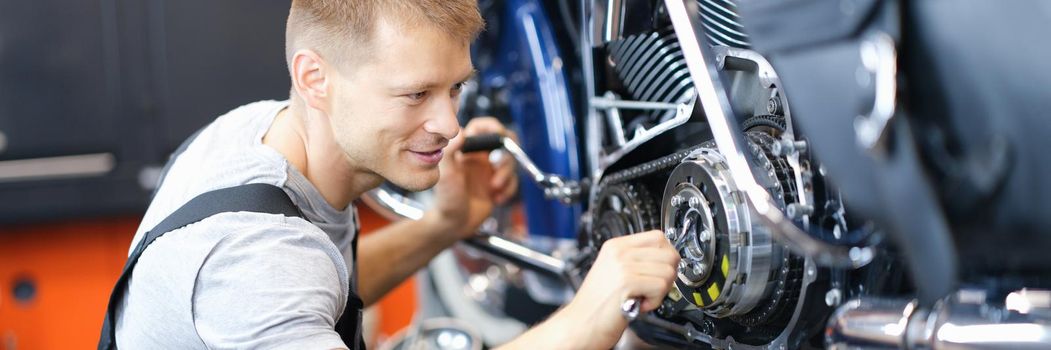 Young male locksmith disassembles motorcycle engine on bench in garage. Motorcycle engine repair concept