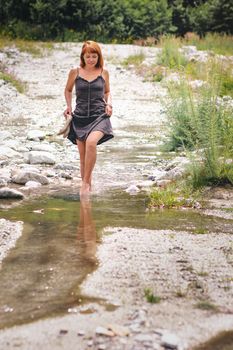 Woman walking by barefoot on river in summertime