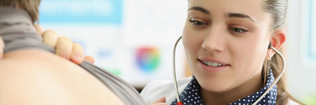 Portrait of young female doctor listen to patients back with stethoscope equipment. Concentrated medical worker examine body, diagnostic. Medicine concept