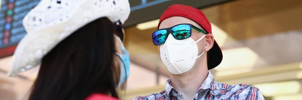 Portrait of couple going on vacation during pandemic wait for their flight in airport. Man and woman wear protective face masks. Virus, holiday concept