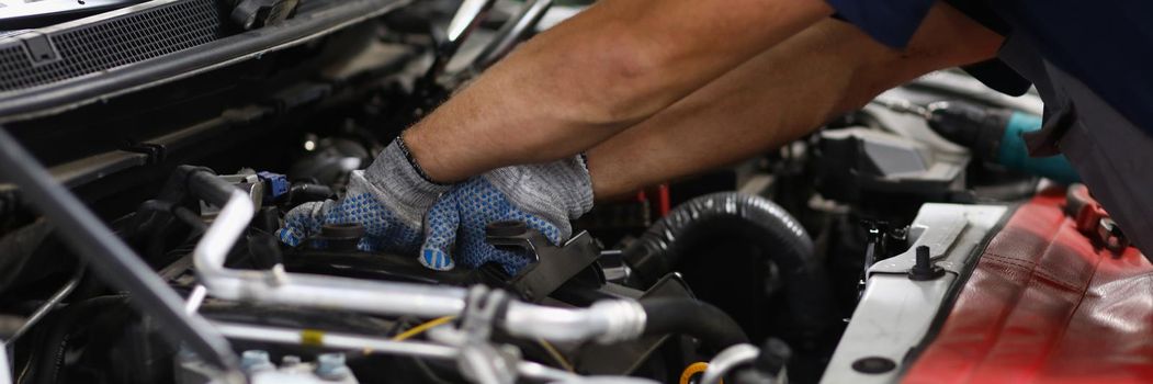 Close-up of professional mechanic male repair detail in automobile on pit station. Qualified garage worker in uniform fix car. Maintenance service concept