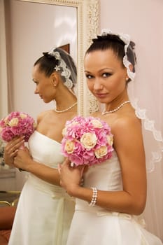 Bride is getting ready for the ceremony in front of the mirror and holding a bouquet.