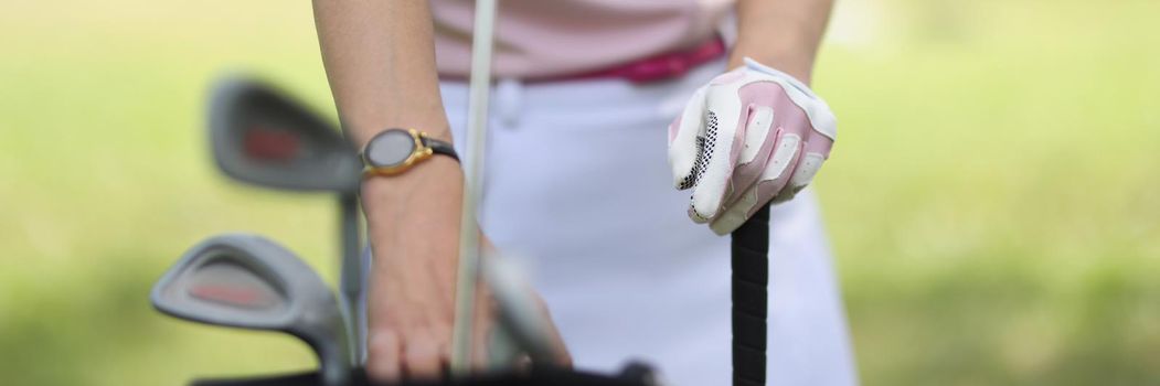 Close-up of professional female golf player choosing golf club from bag. Green field behind for perfect game. Competition, sport, physical activity concept