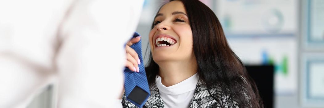 Portrait of businesswoman flirting with corporate male worker touching his tie and laughing. Female boss start relationship at work. Office romance concept