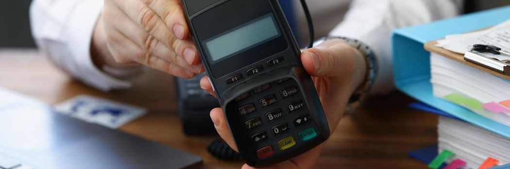Close-up of man holding modern credit card reader machine for cashless payment. Empty screen for total cost and numbers on pad. Modern technology concept