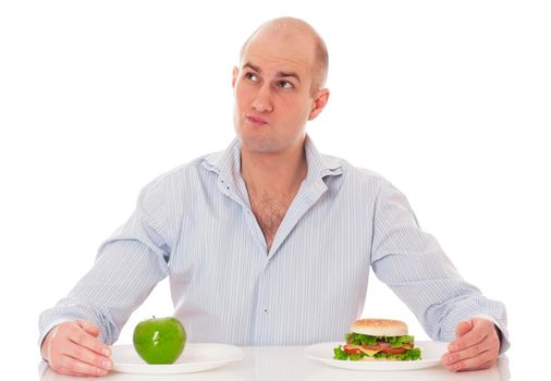 Caucasian man undecided if he is gonna go for the apple or for the hamburger, isolated on white background.