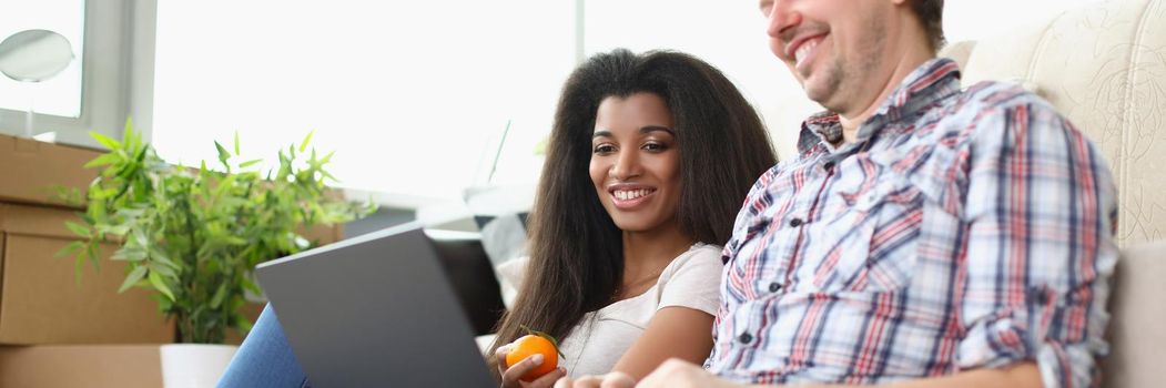 Portrait of friends sitting on carpet floor watching movie on laptop and laughing. Latino american woman eat apple. Spare time, friendship, leisure concept