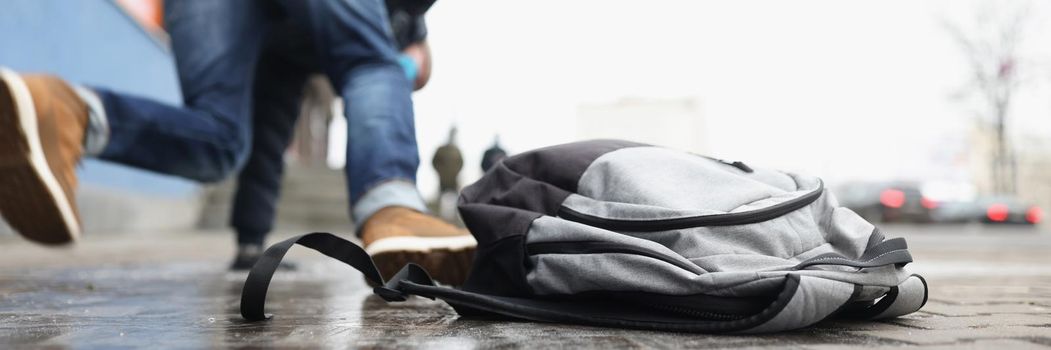 Close-up of person get injury after falling on slippery ground in winter season. Personal backpack lay on asphalt ice. Accident, trauma, clumsy concept