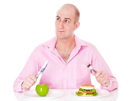 Caucasian man undecided if he is gonna go for the apple or for the hamburger, isolated on white background.