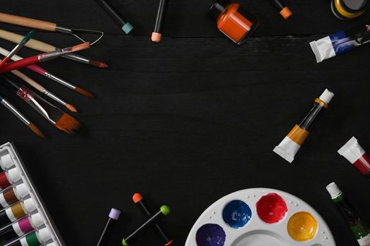 Flat lay watercolors, palette and paint brushes on black wooden table. Artist or designer workplace.