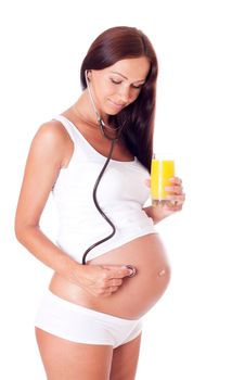 Pregnant woman holding glass of juice and listening to her baby with a stethoscope. Isolated on white.