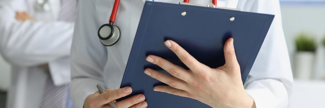 Close-up of medical coworkers in uniform posing in clinic with prescription paper. Professional hospital workers examine patients history. Medicine concept