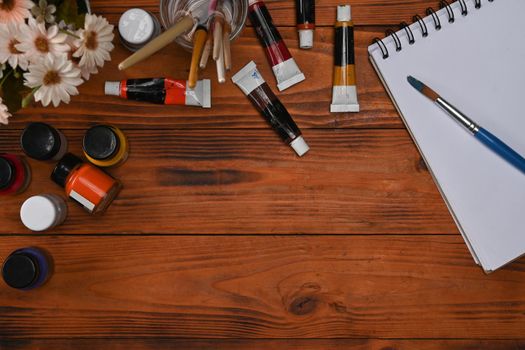 Blank notepad, paint brushes and watercolors on wooden background. Artistic background, top view, flat lay.