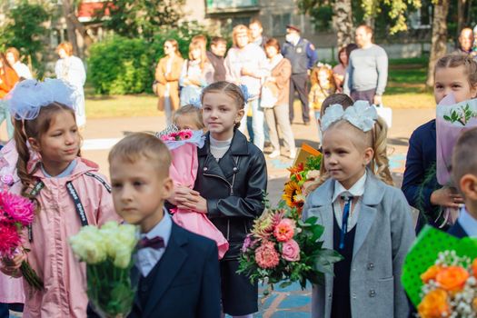 NOVOKUZNETSK, KEMEROVO REGION, RUSSIA - SEP, 1, 2021: Meeting with the first-grade pupils and teacher at schoolyard. The day of knowledge in Russia.