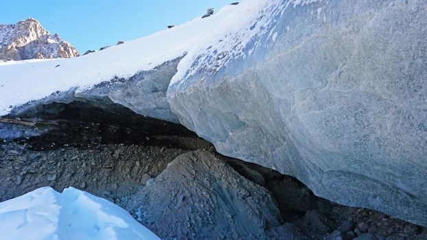 Ice cave in the snowy mountains. Tuyuk-Su glacier. Black ice reflects everything like a mirror. The ledge of stones collapsed. huge cracks in the ice tunnel. Snowy mountains of Almaty, Kazakhstan.